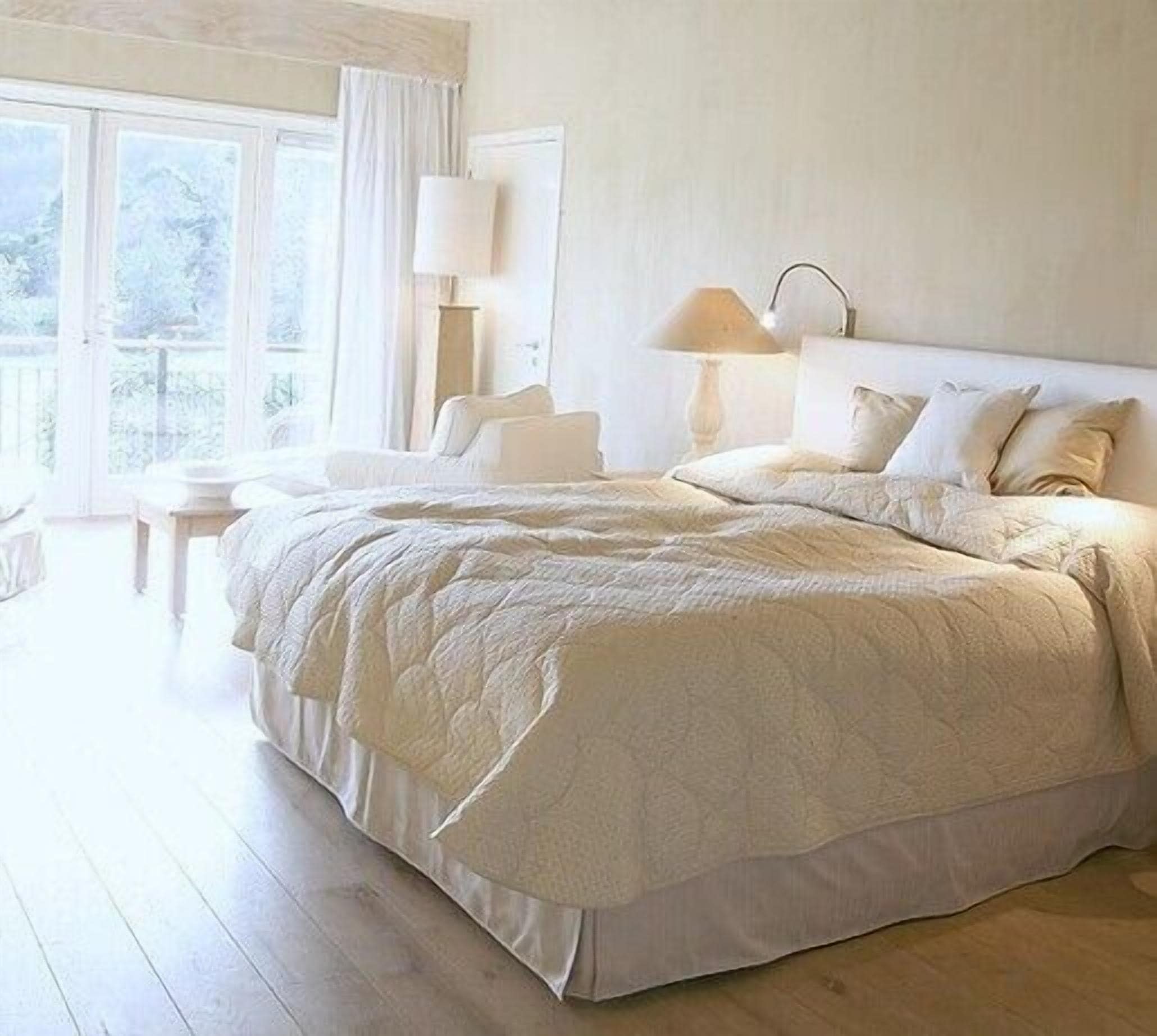 A spacious bedroom with a large bed, a nightstand, a lamp, and a view of the outdoors through a large window.