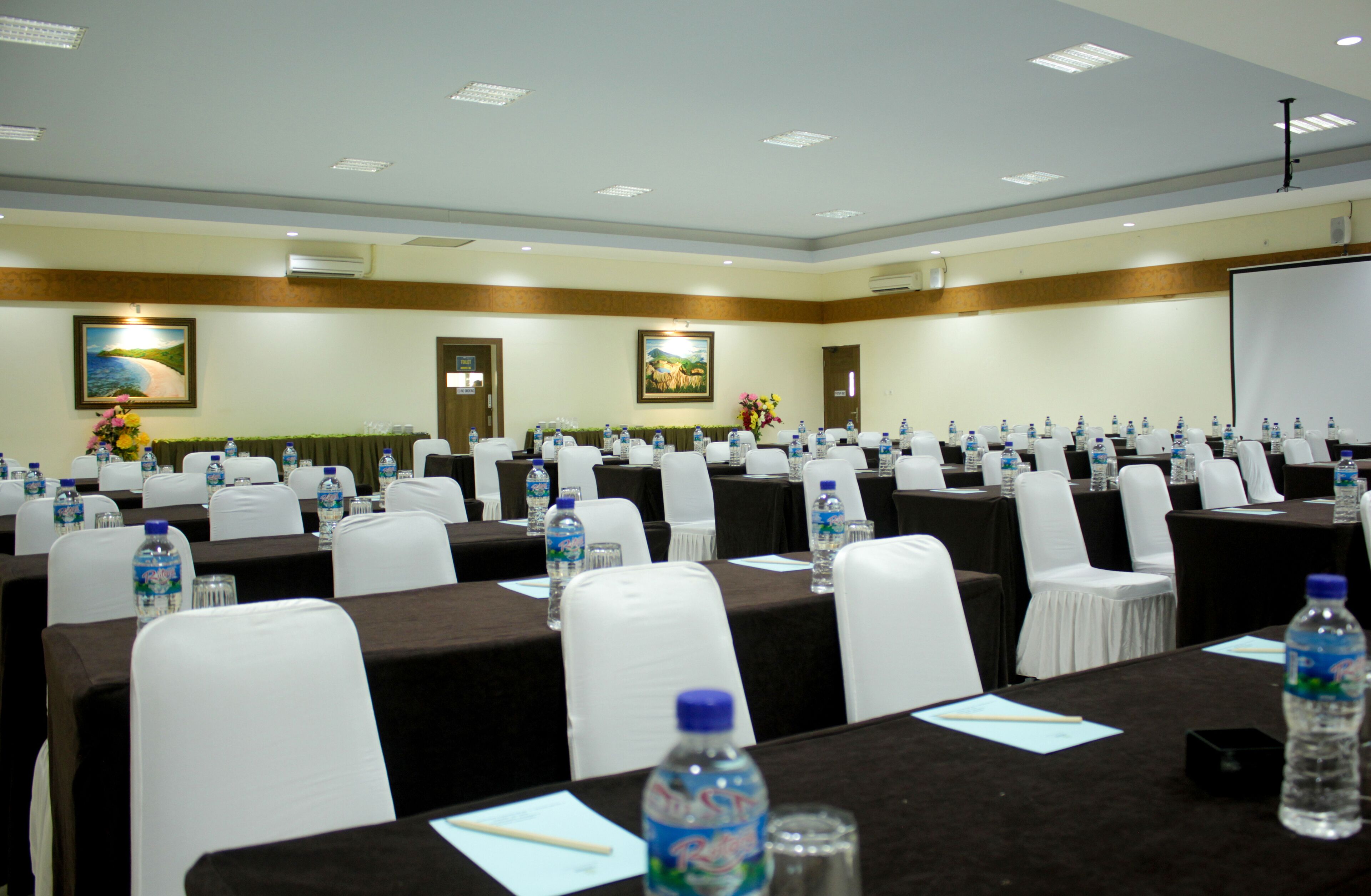 Un salón de conferencias con filas de mesas, cada una con botellas de agua y tarjetas de identificación.