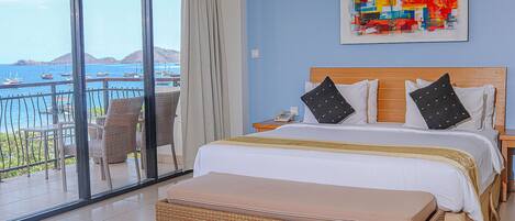 A bedroom with a large bed, a view of the sea, and a colorful abstract painting on the wall.