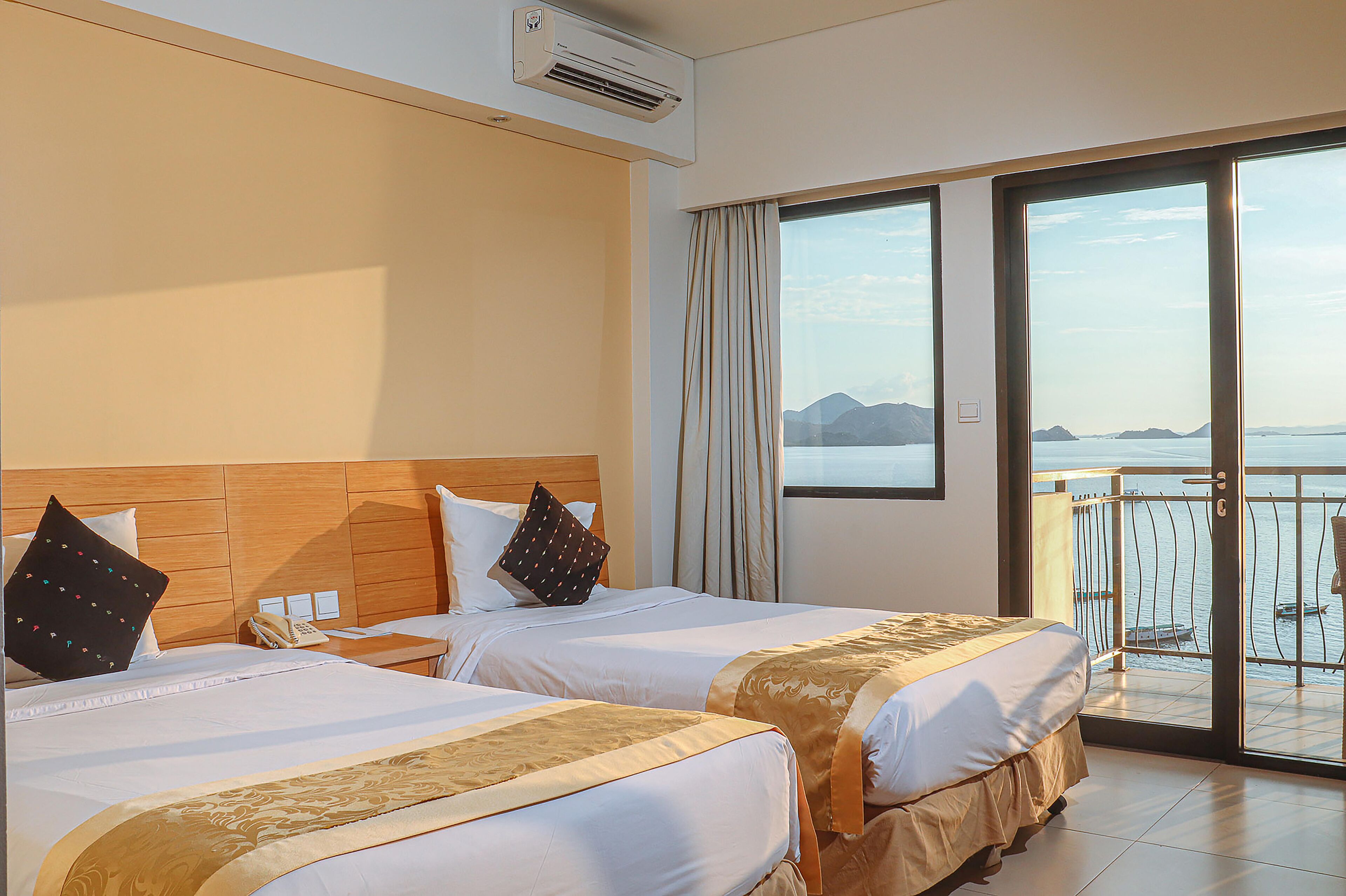 A hotel room with two beds, a balcony with a view of the sea, and an air conditioning unit on the wall.