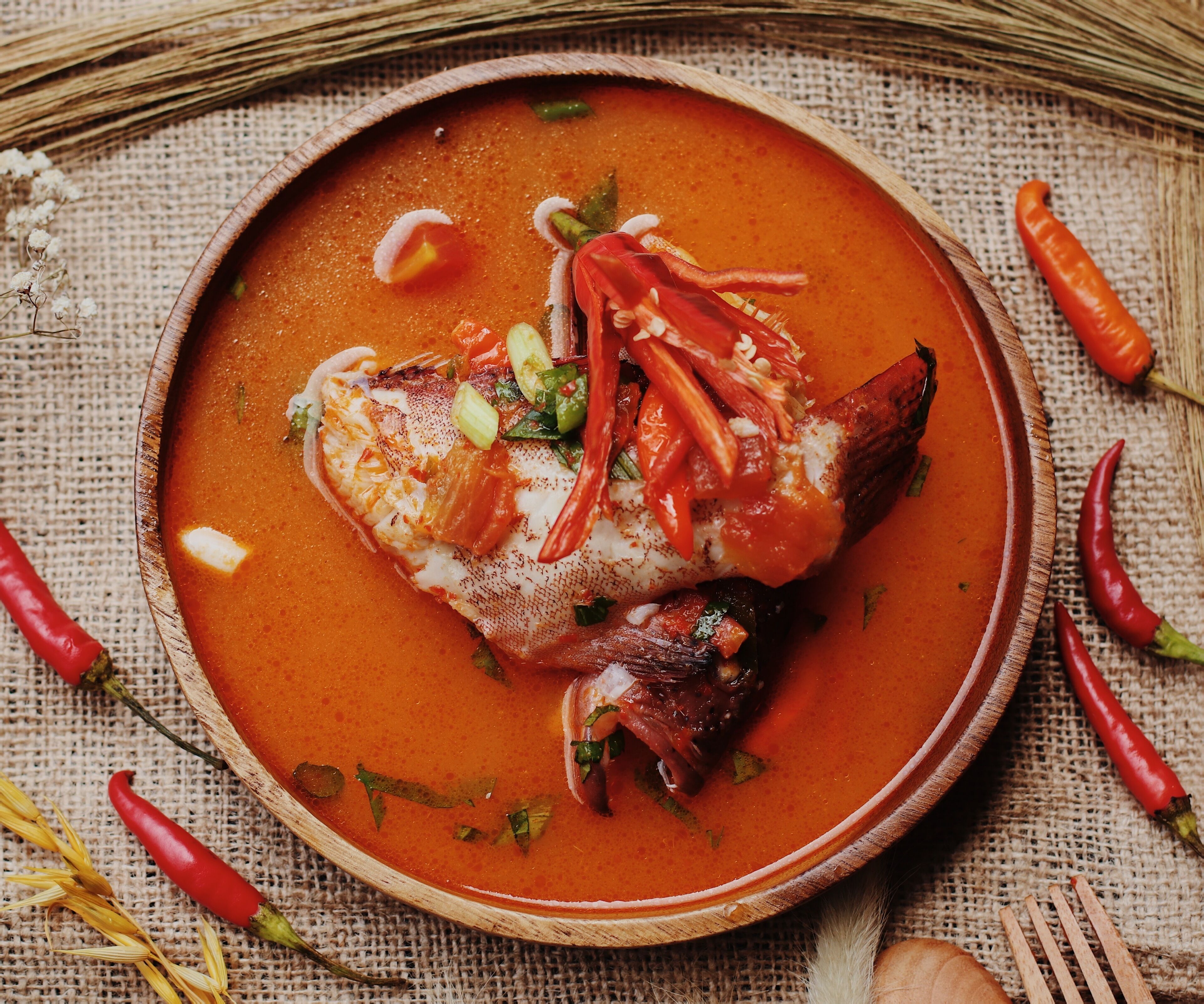 A fish dish in a bowl with red chili peppers and herbs.
