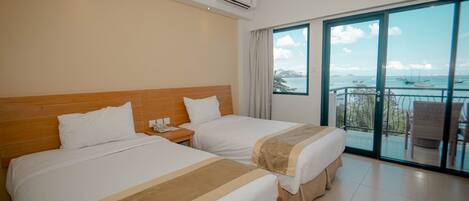 A hotel room with two beds, a nightstand, an air conditioning unit, and a balcony with a view of the sea.