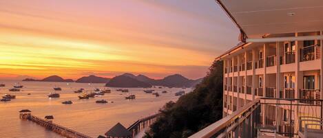 Un hotel con balcón con vistas a un puerto deportivo al atardecer.