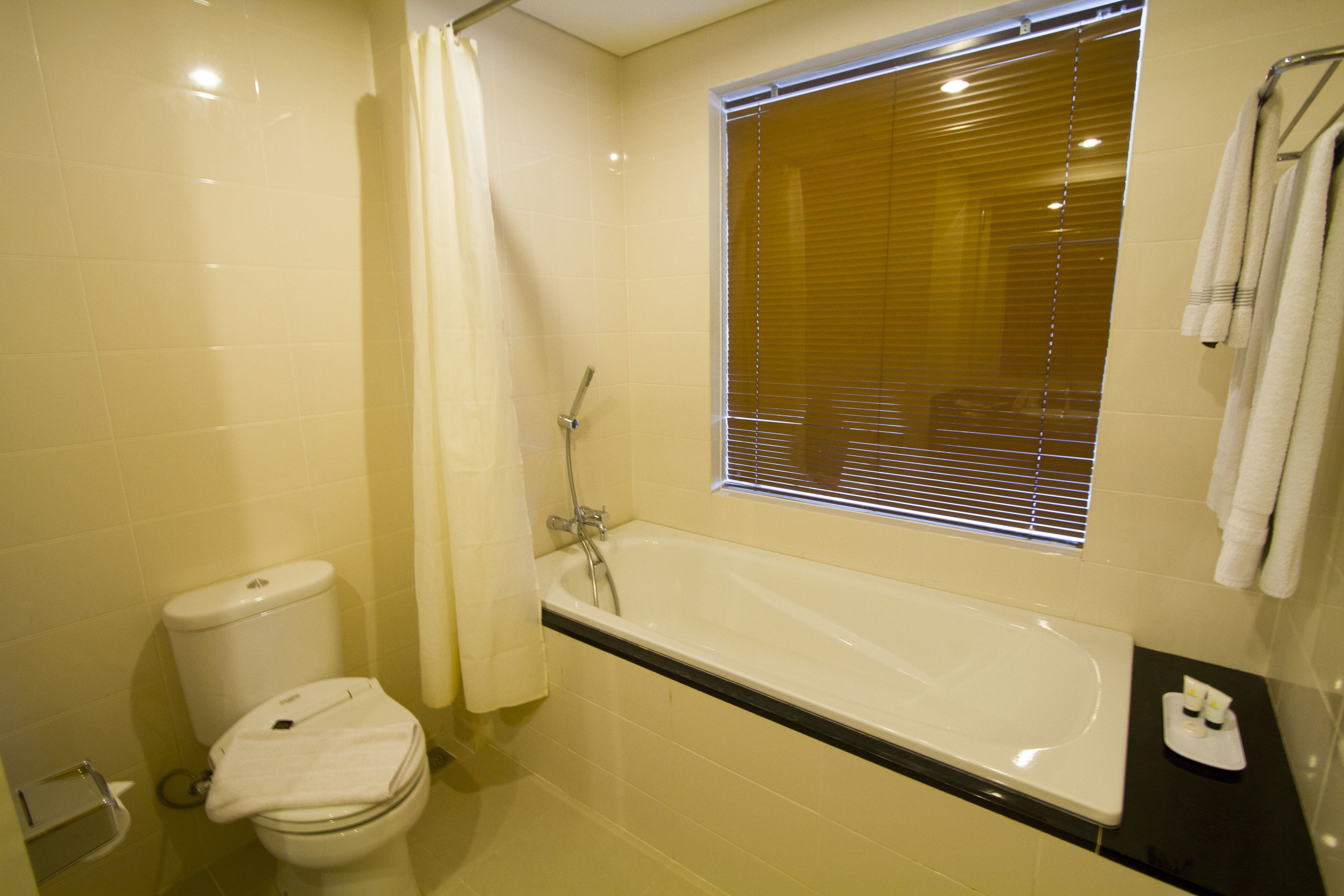Une salle de bain avec une baignoire, des toilettes et une fenêtre équipée de stores.