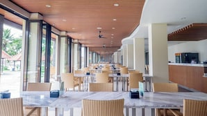 A spacious indoor dining area with wooden ceiling and large windows, featuring tables and wicker chairs. - LAPRIMA Hotel Flores (Labuan Bajo)
