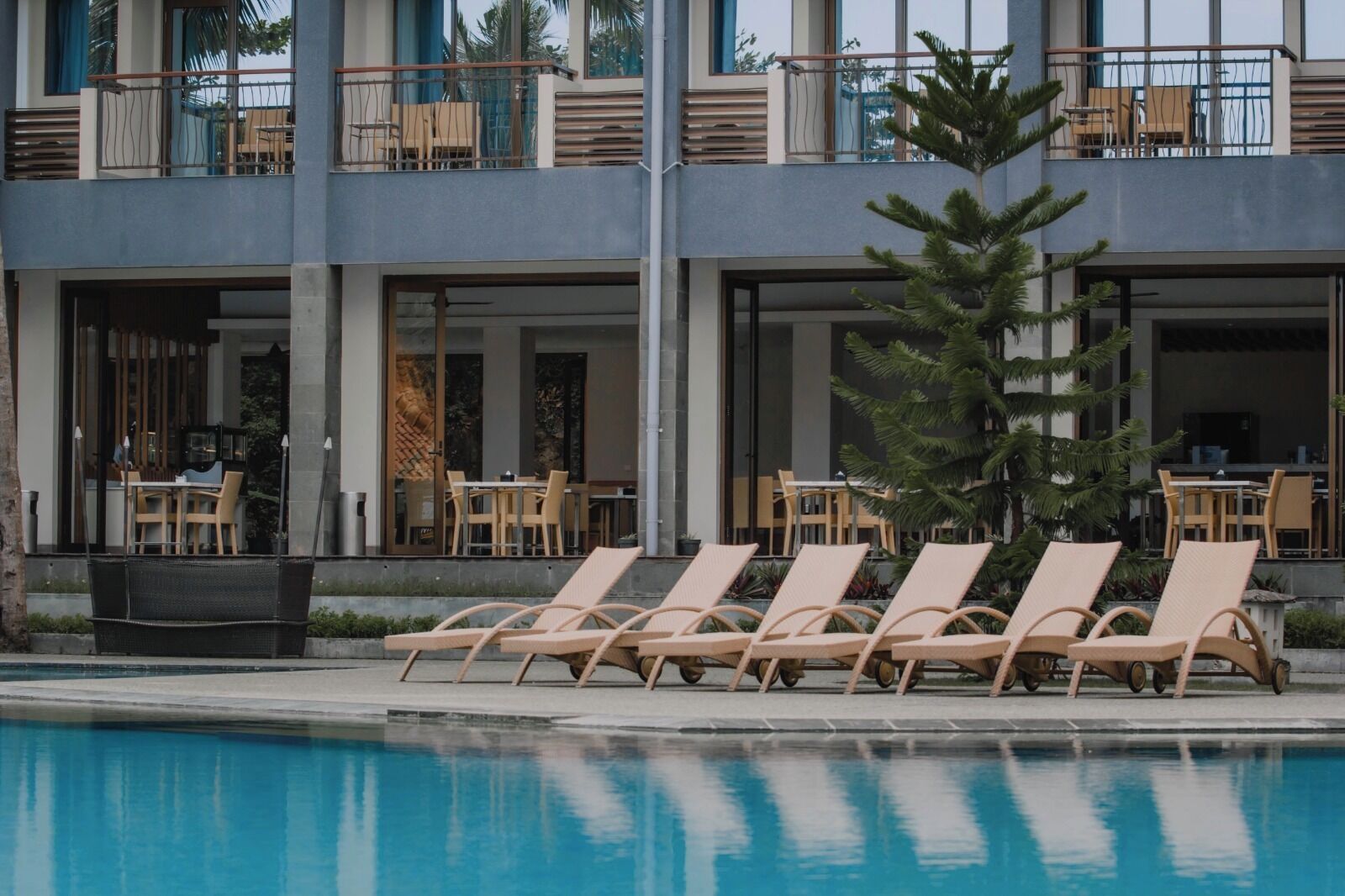 A modern hotel with a pool area featuring lounge chairs and tables.