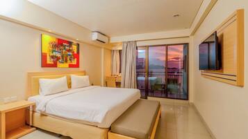 Habitación de hotel con una cama grande, un escritorio, un televisor y un balcón con vista al atardecer.