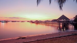 A beach with overwater bungalows and a pier extending into calm waters. - LAPRIMA Hotel Flores (Labuan Bajo)