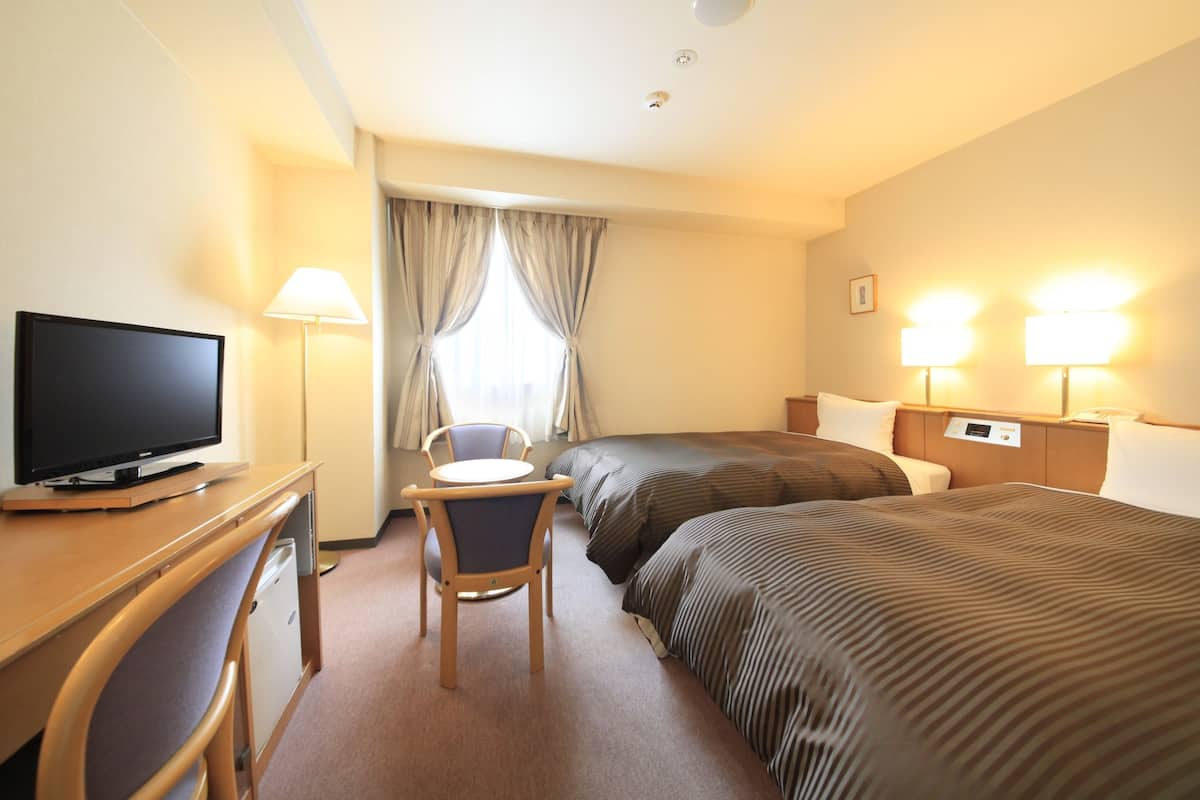 Une chambre d’hôtel comprenant un lit, un bureau avec une télévision, une chaise et deux lampes de chevet.