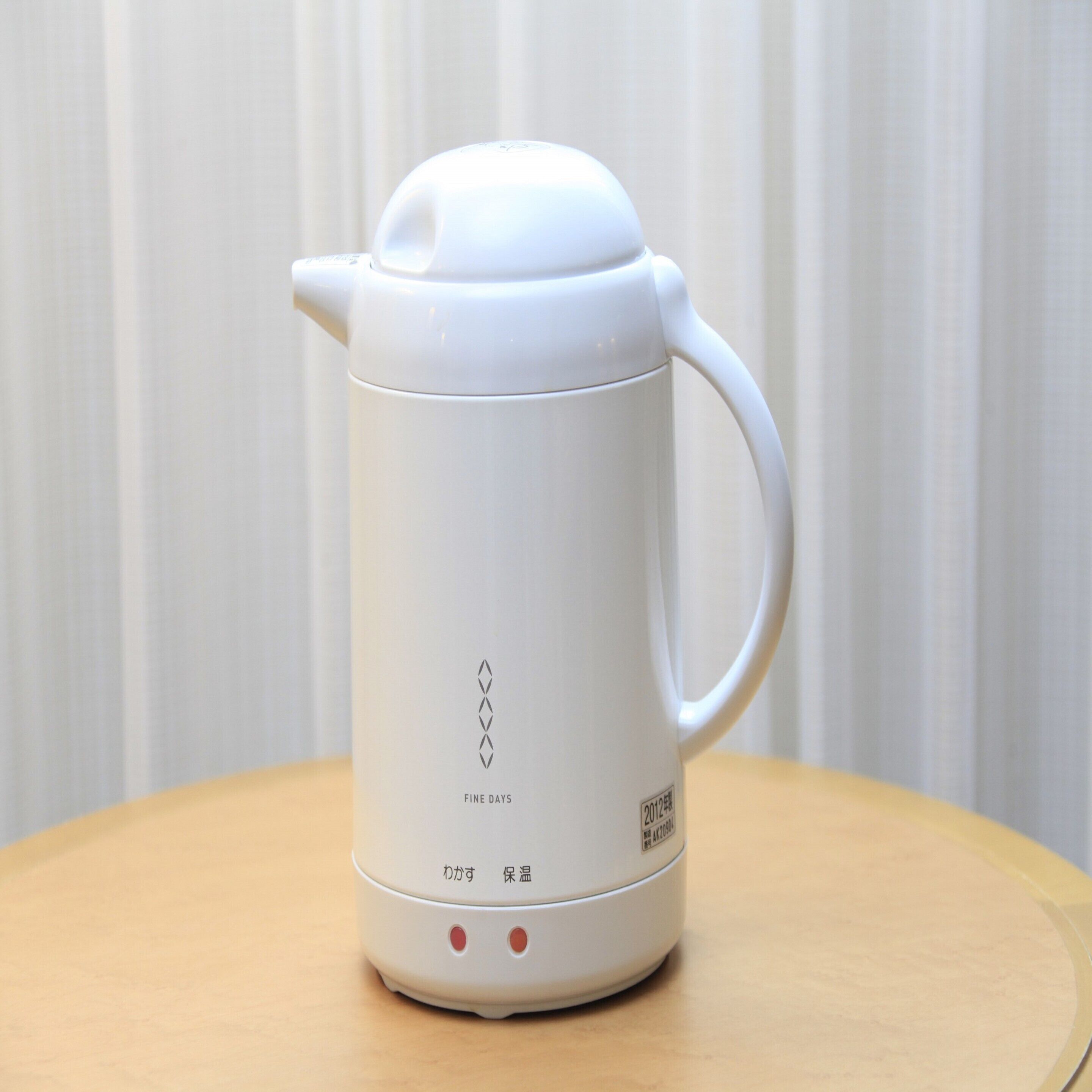 A white electric kettle with a lid, placed on a wooden table.