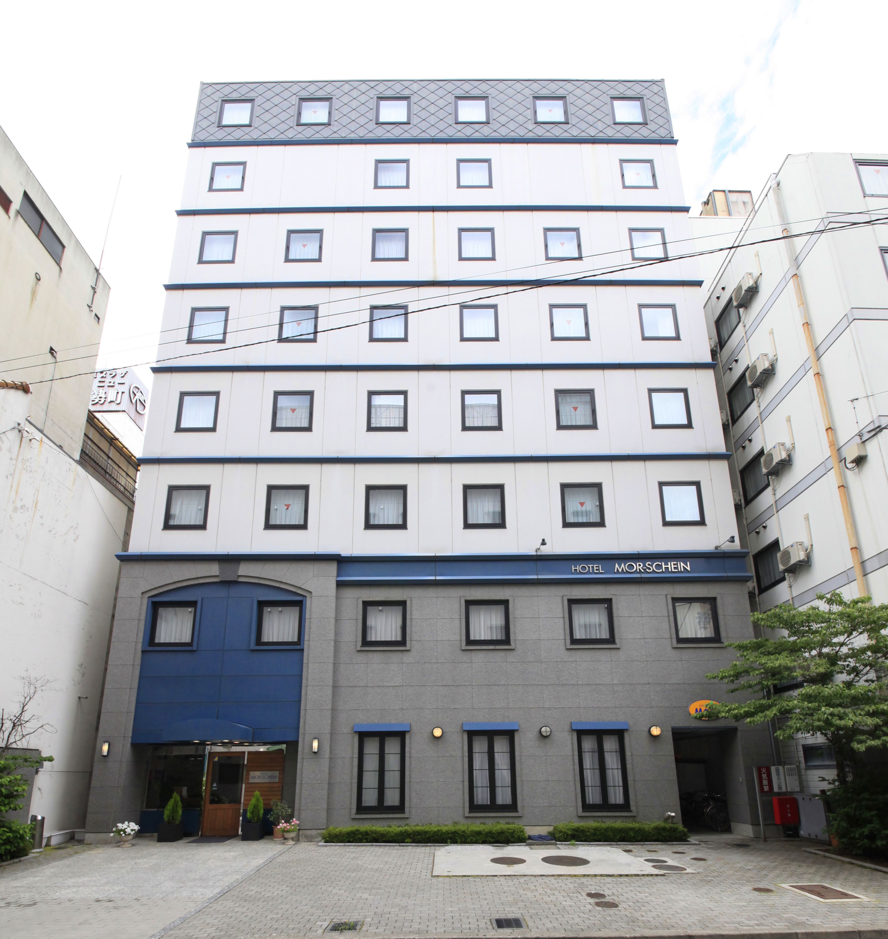 A multi-story hotel with a blue entrance, multiple windows, and a sign indicating it is the Hotel Morschein.