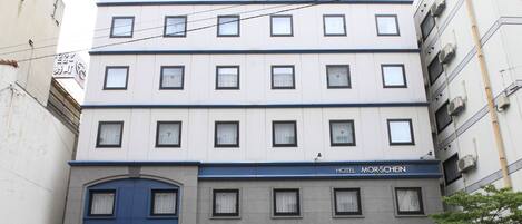 A multi-story hotel with a blue entrance, multiple windows, and a sign indicating it is the Hotel Morschein.
