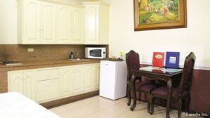 Una cocina con armarios blancos, un microondas, un refrigerador y una mesa de comedor con sillas. Hay un cuadro enmarcado en la pared sobre la mesa.