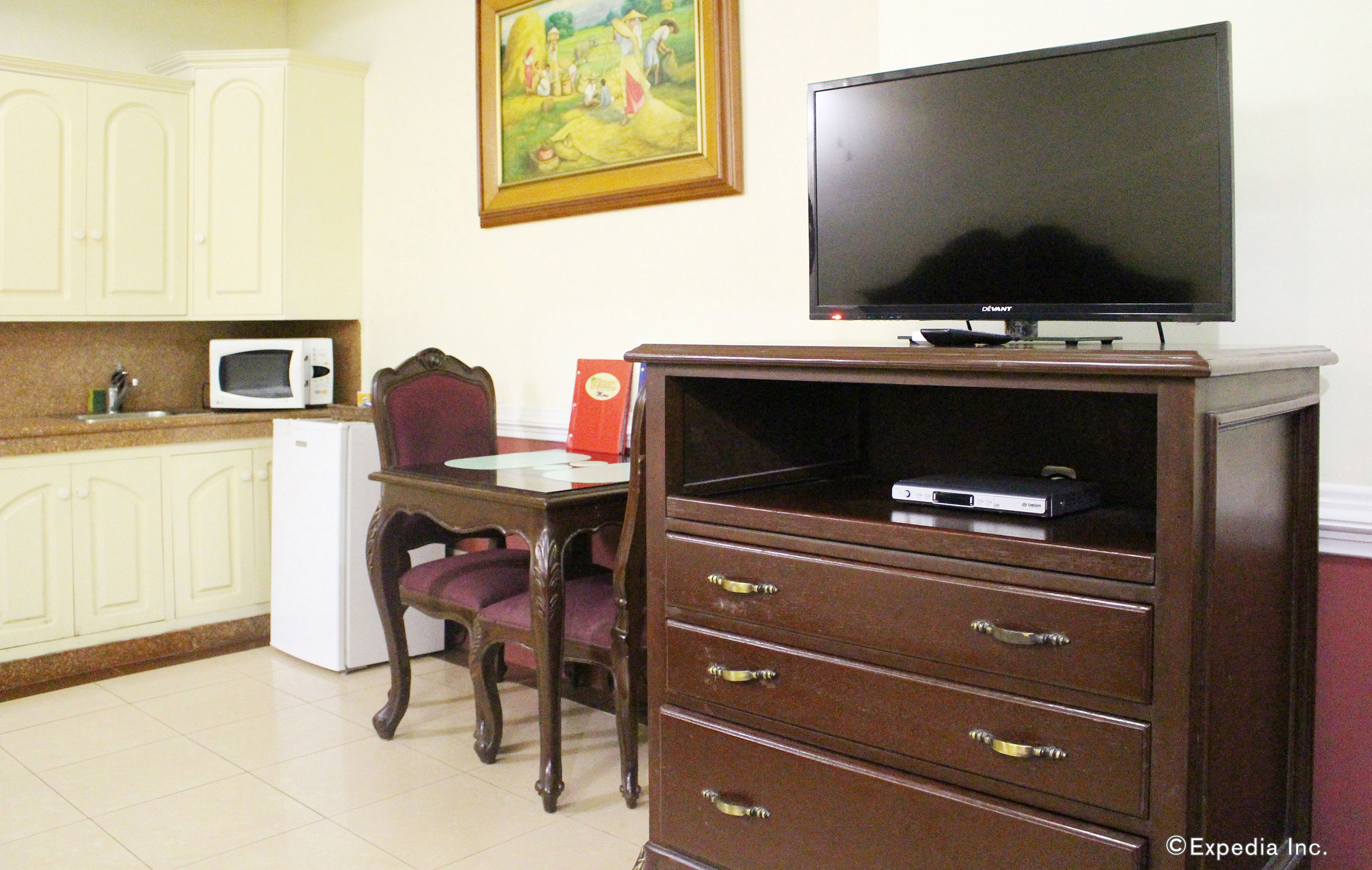 Una habitación con una mesa de comedor, sillas, un televisor sobre un mueble bajo, un microondas y armarios.