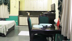 Habitación de hotel compacta con cama, una mesa de comedor con sillas, una pequeña zona de cocina y un ventilador de techo.