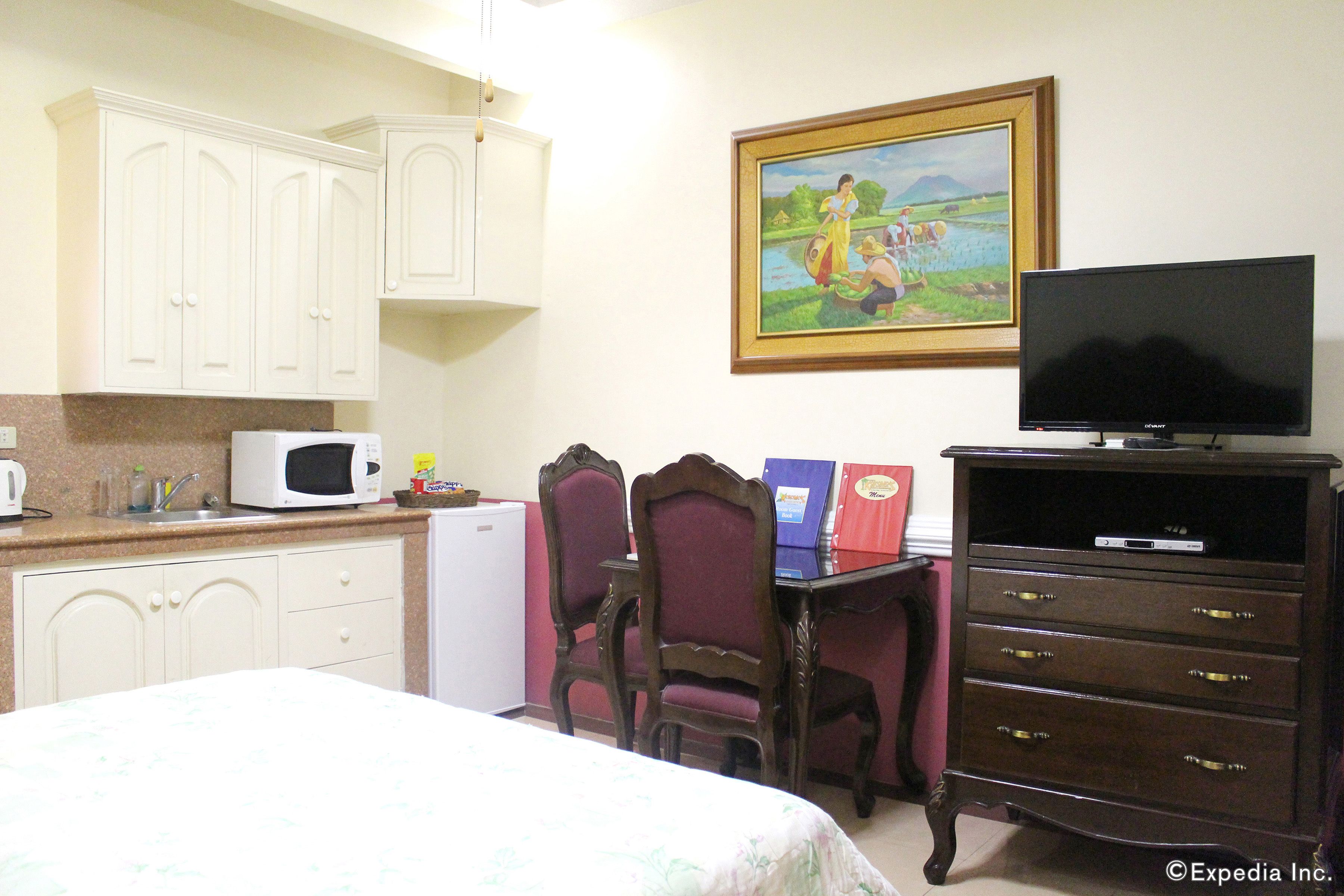 A hotel room with a bed, a desk with a computer, a television, a microwave, and a refrigerator.