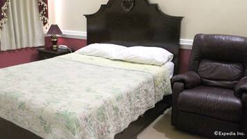 A neatly made bed with a floral bedspread, a dark wooden headboard, a brown leather chair, and a nightstand with a lamp and phone.