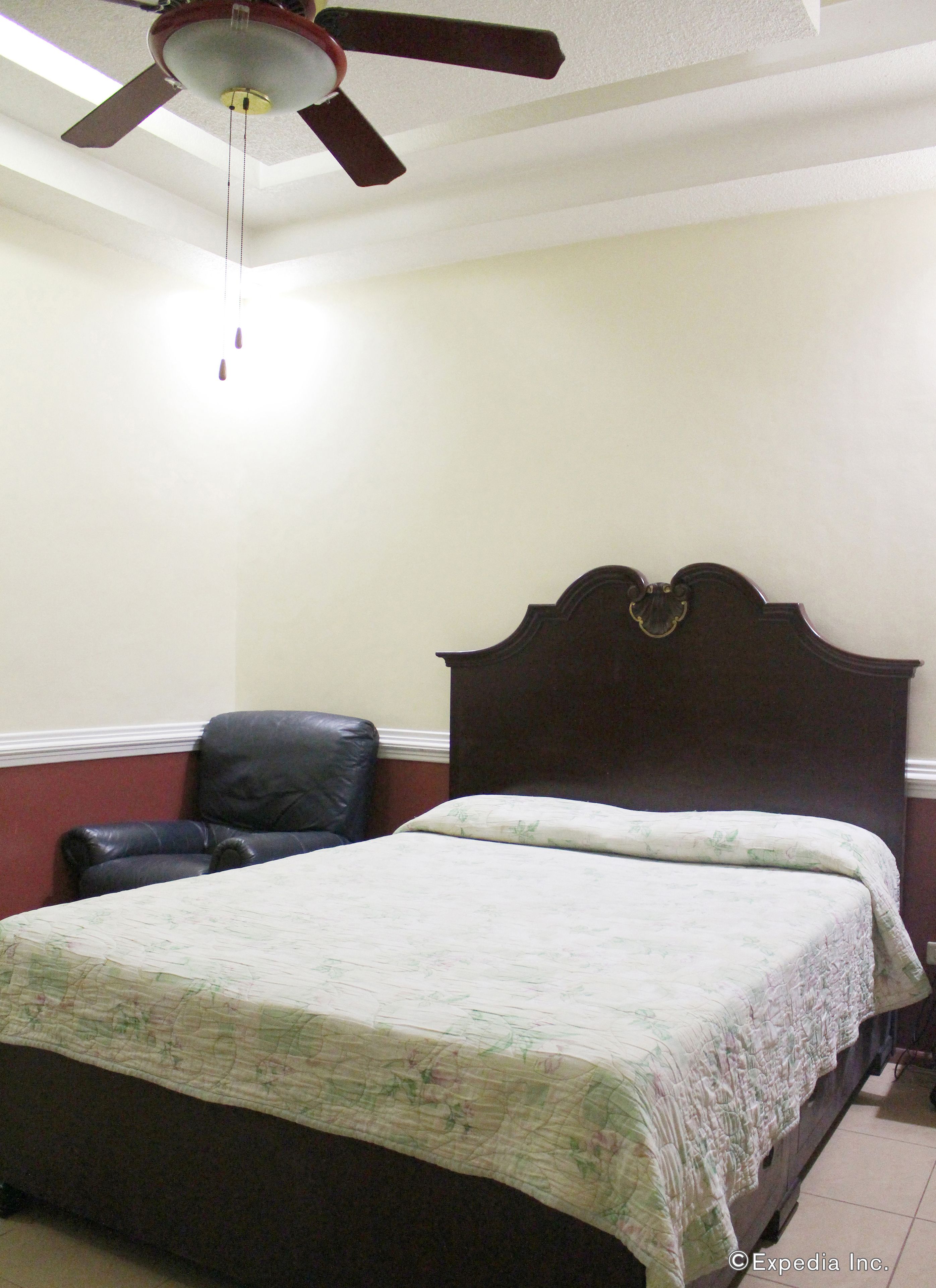 A bedroom with a bed, a chair, a ceiling fan, and a light fixture.