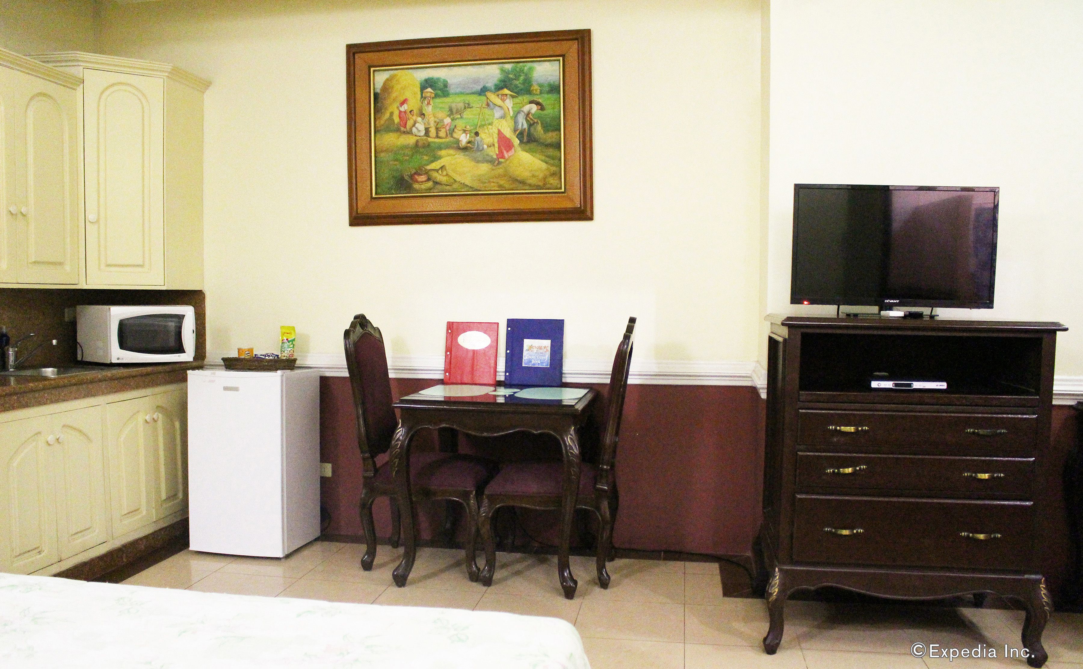 A hotel room with a bed, a desk with a computer, a TV, a microwave, and a painting on the wall.