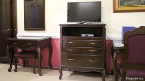 Una habitación con un armario de madera, un televisor encima y un escritorio con cajones.