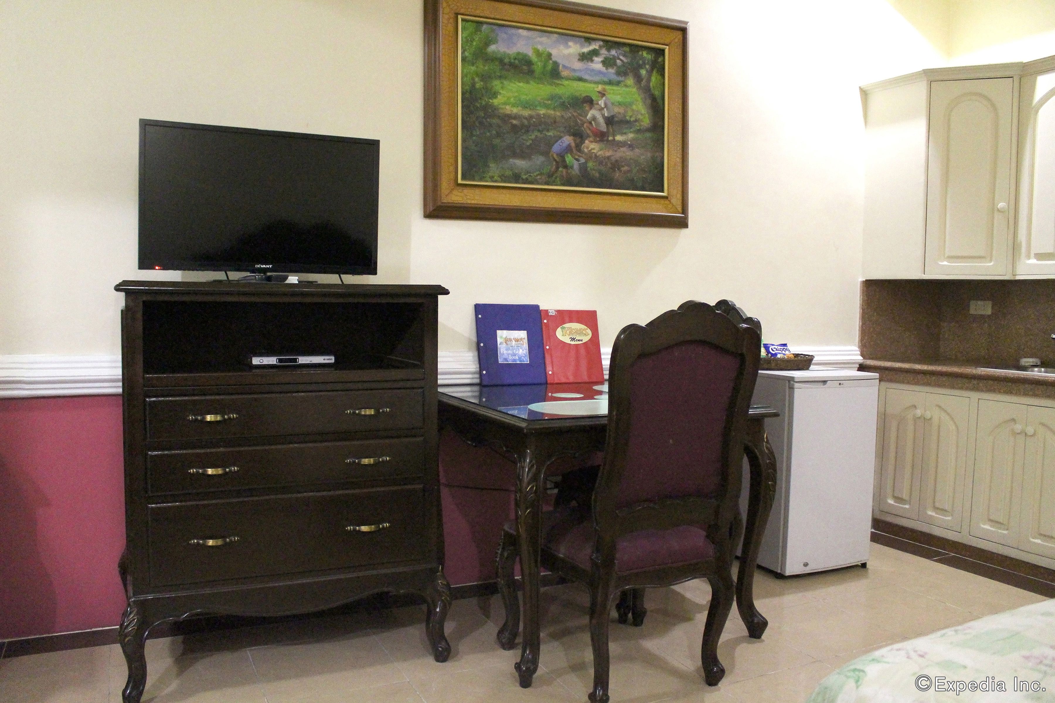 A room with a desk, chair, television, cabinets, and a small refrigerator.