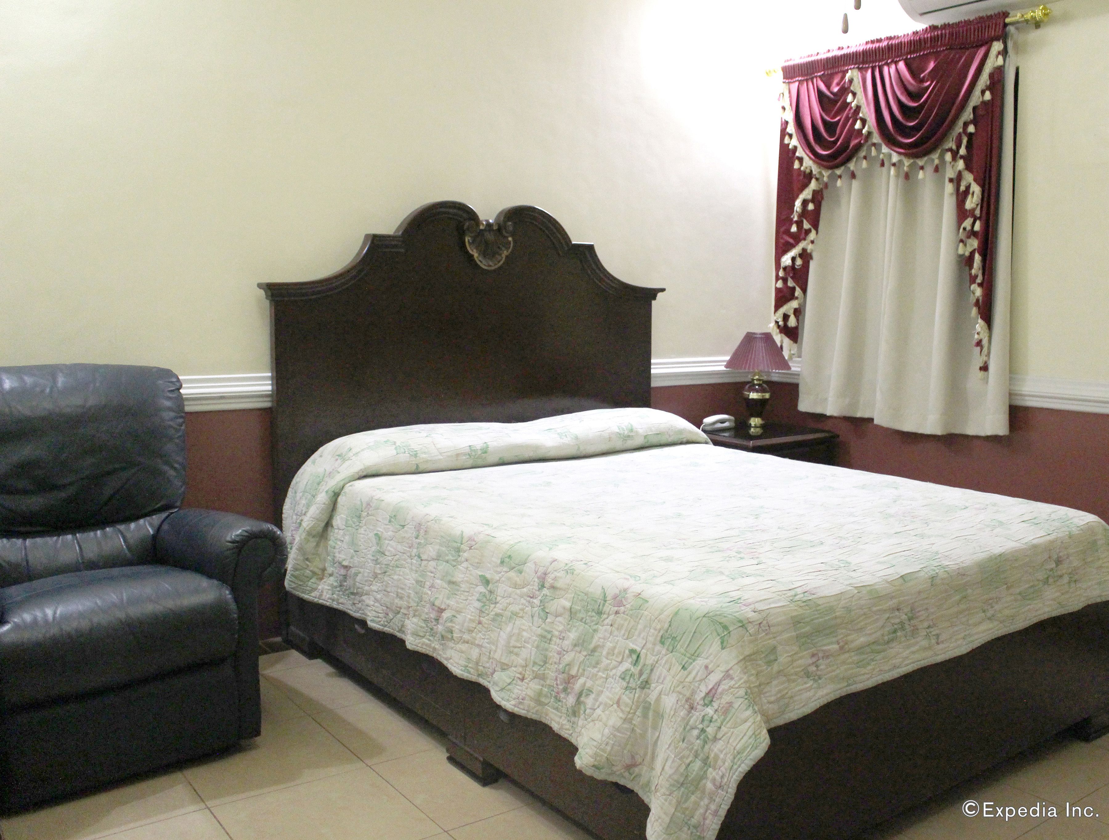 A bedroom with a bed, a chair, a nightstand, and a window with curtains.