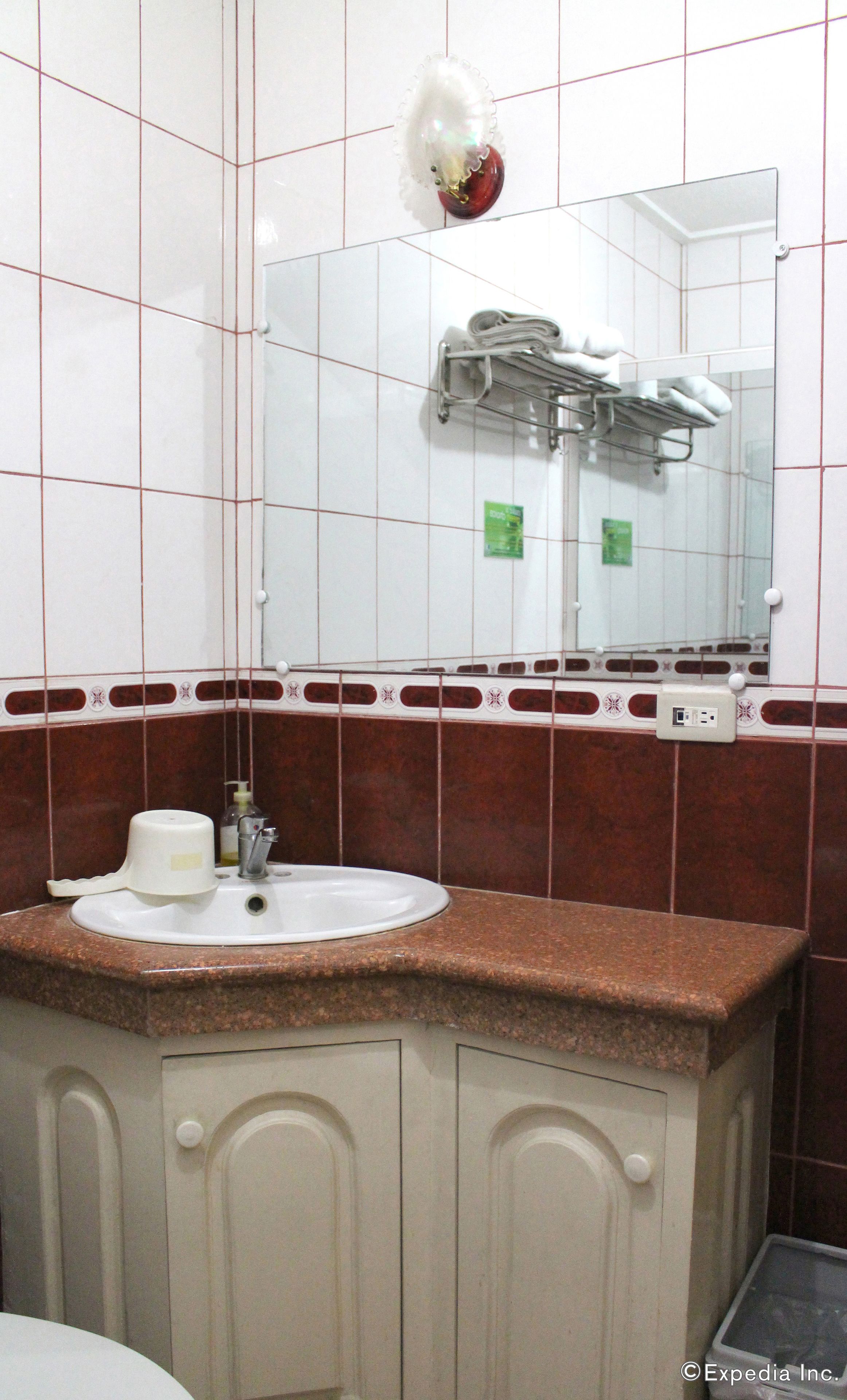 A bathroom with a sink, mirror, towel rack, and a soap dispenser.