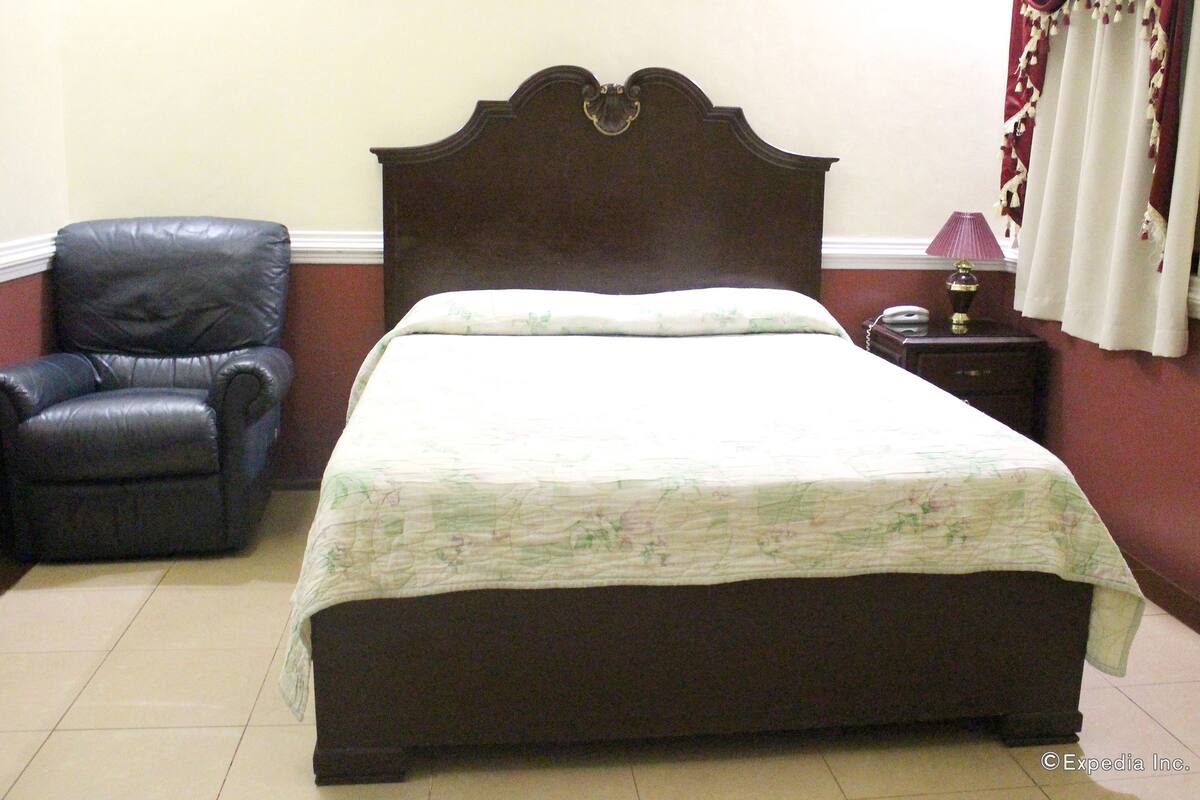 Une chambre à coucher avec un grand lit, un fauteuil en cuir, une table de chevet avec une lampe et un rideau.