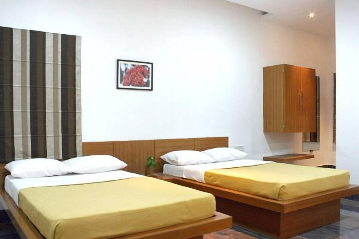 Una habitación de hotel con dos camas individuales, un cabecero de madera, una mesita pequeña y un armario.