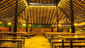 An indoor dining area with wooden tables and benches, a high ceiling with a grid pattern, and a view of greenery outside. - Dream Valley Resort (Hyderabad)