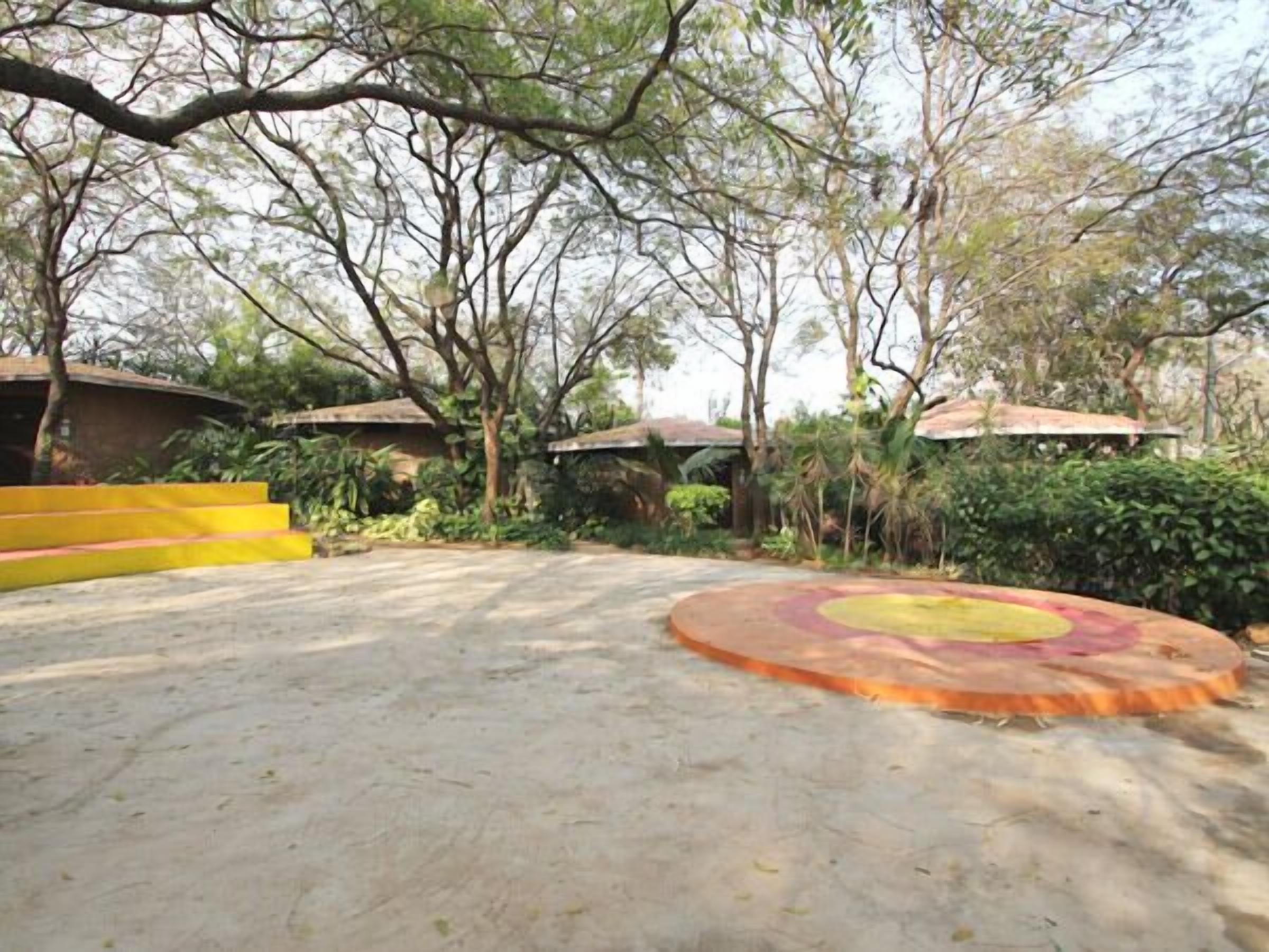 Un patio con una zona de estar circular al aire libre, escalones que conducen a un edificio y abundante vegetación circundante.