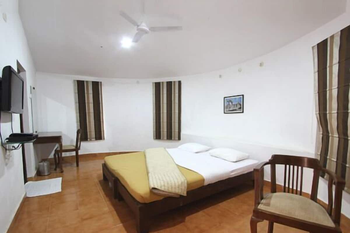 Habitación de hotel con cama, escritorio, silla, ventilador de techo y ventana con persianas.
