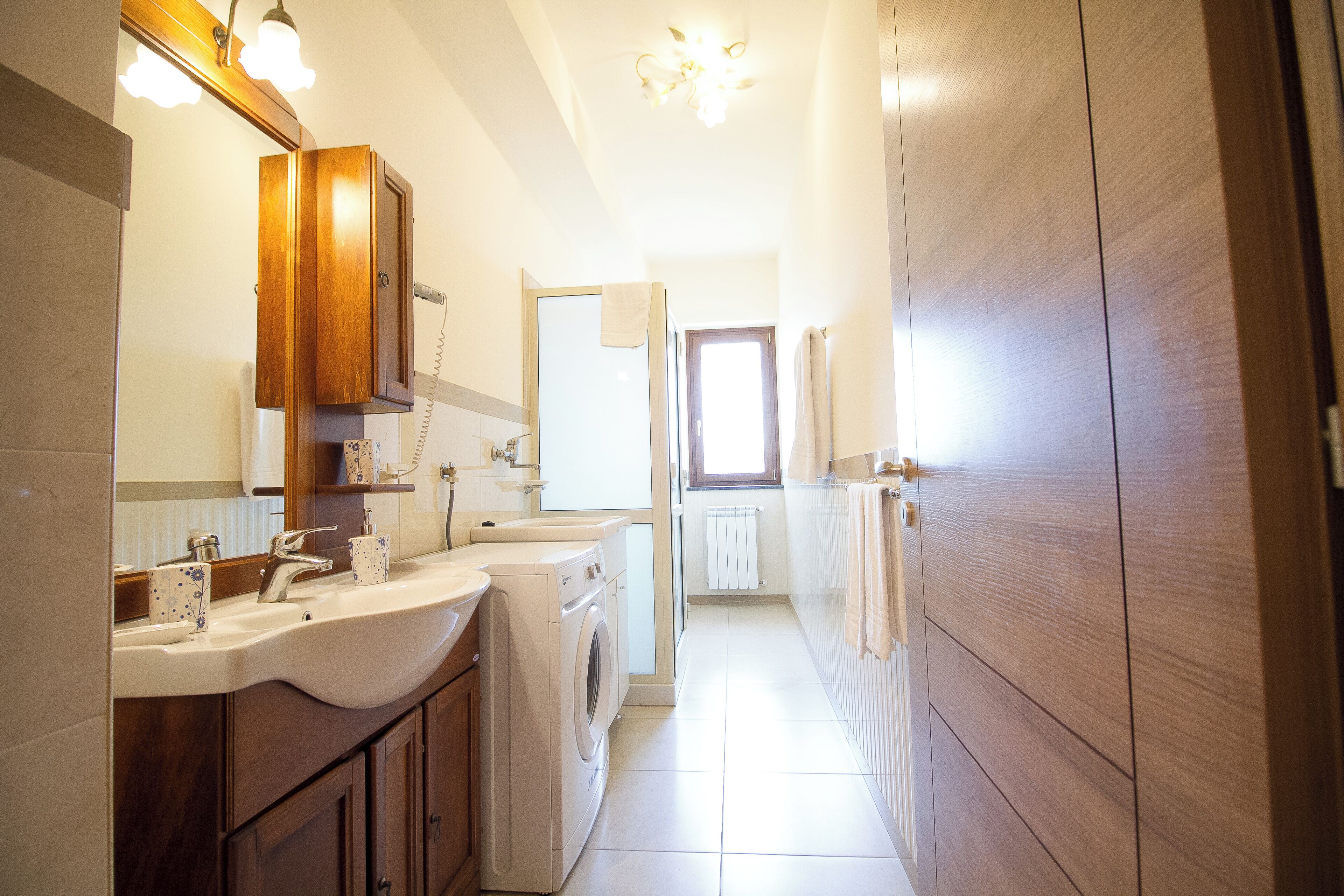 Un baño moderno con un espejo grande, dos lavamanos, una lavadora y armarios de madera.