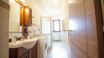 Un baño moderno con un espejo grande, dos lavamanos, una lavadora y armarios de madera.