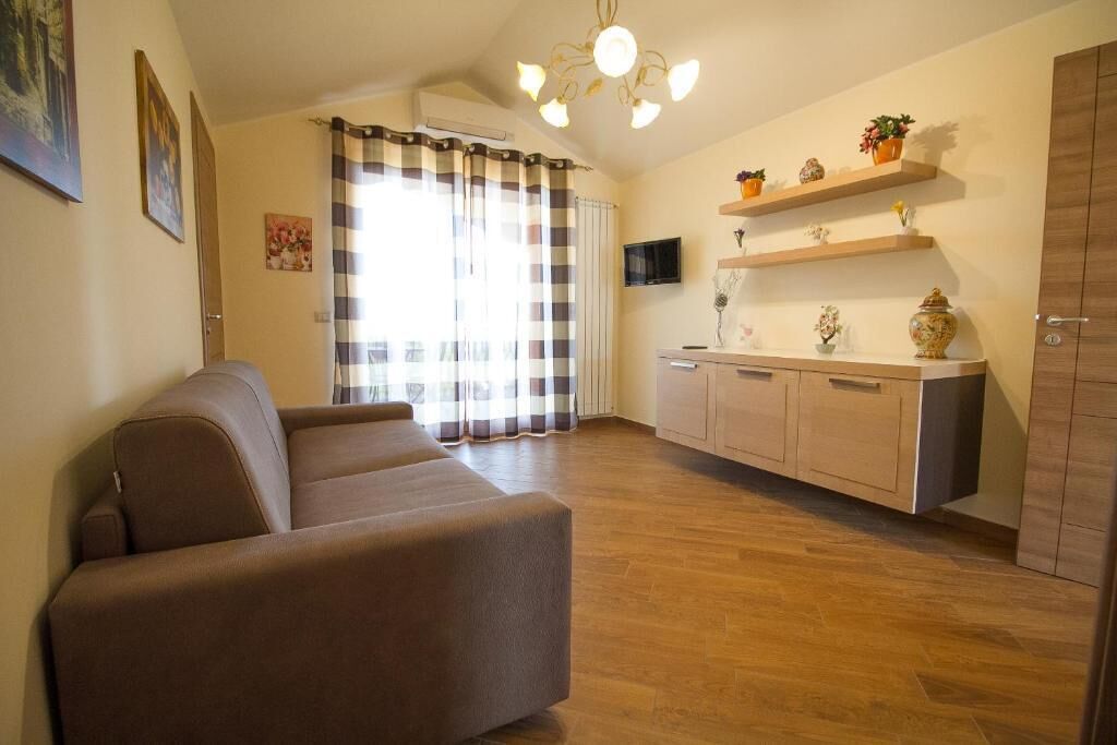 Un salon avec un canapé, un coin cuisine doté de meubles en bois, un téléviseur et une fenêtre avec des rideaux.