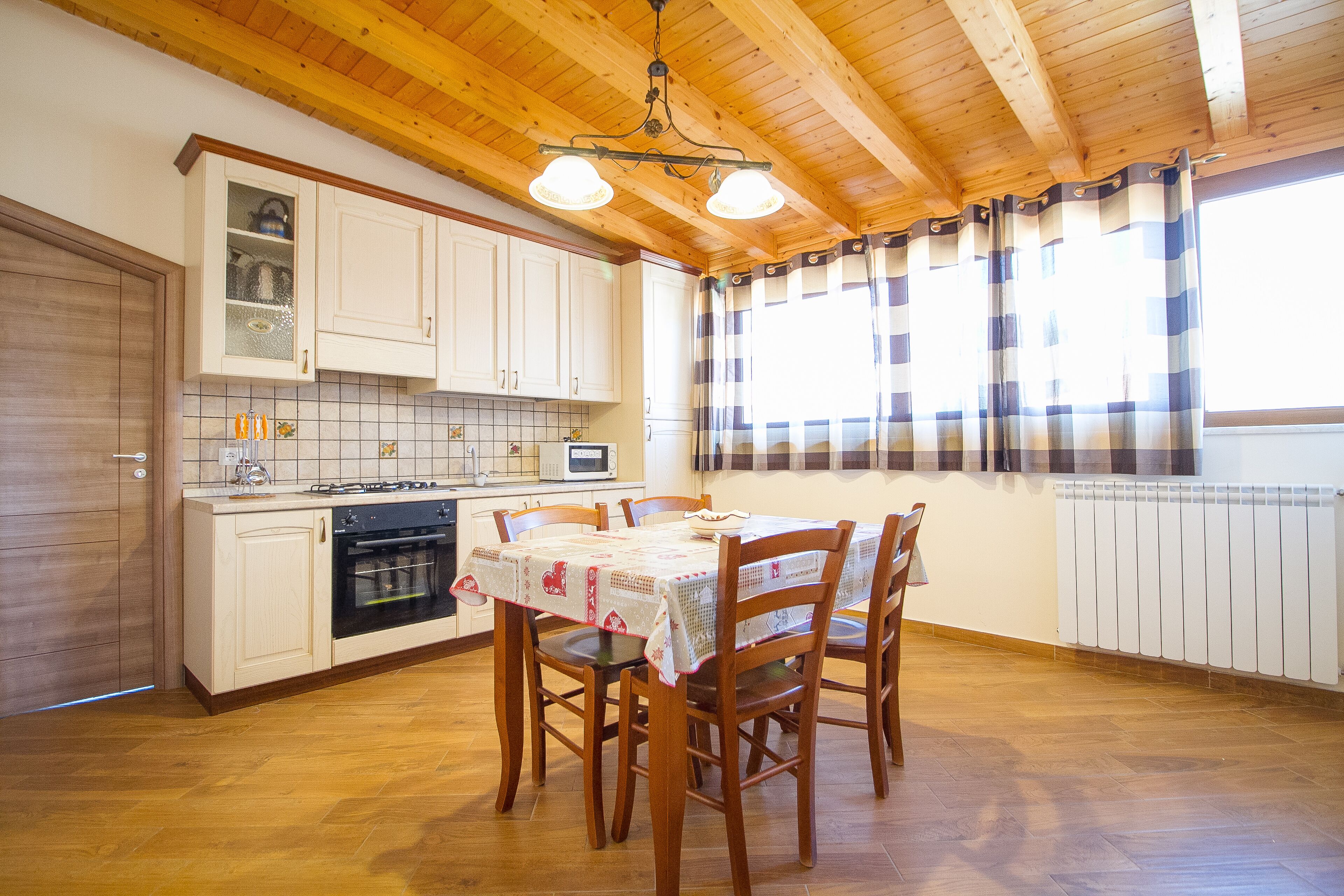 Una cocina con armarios de madera, una mesa de comedor con sillas, una estufa y una ventana con cortinas.