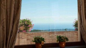 A window with curtains, two potted plants, and a view of a distant landscape.