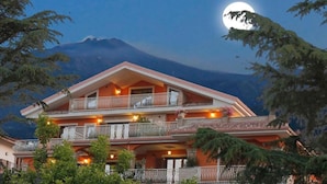 A multi-story hotel with balconies, set against a mountain backdrop.