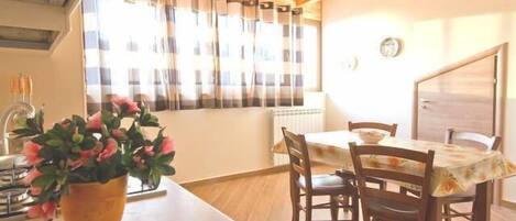 A dining area with a table and chairs, a potted plant, and a window with curtains.