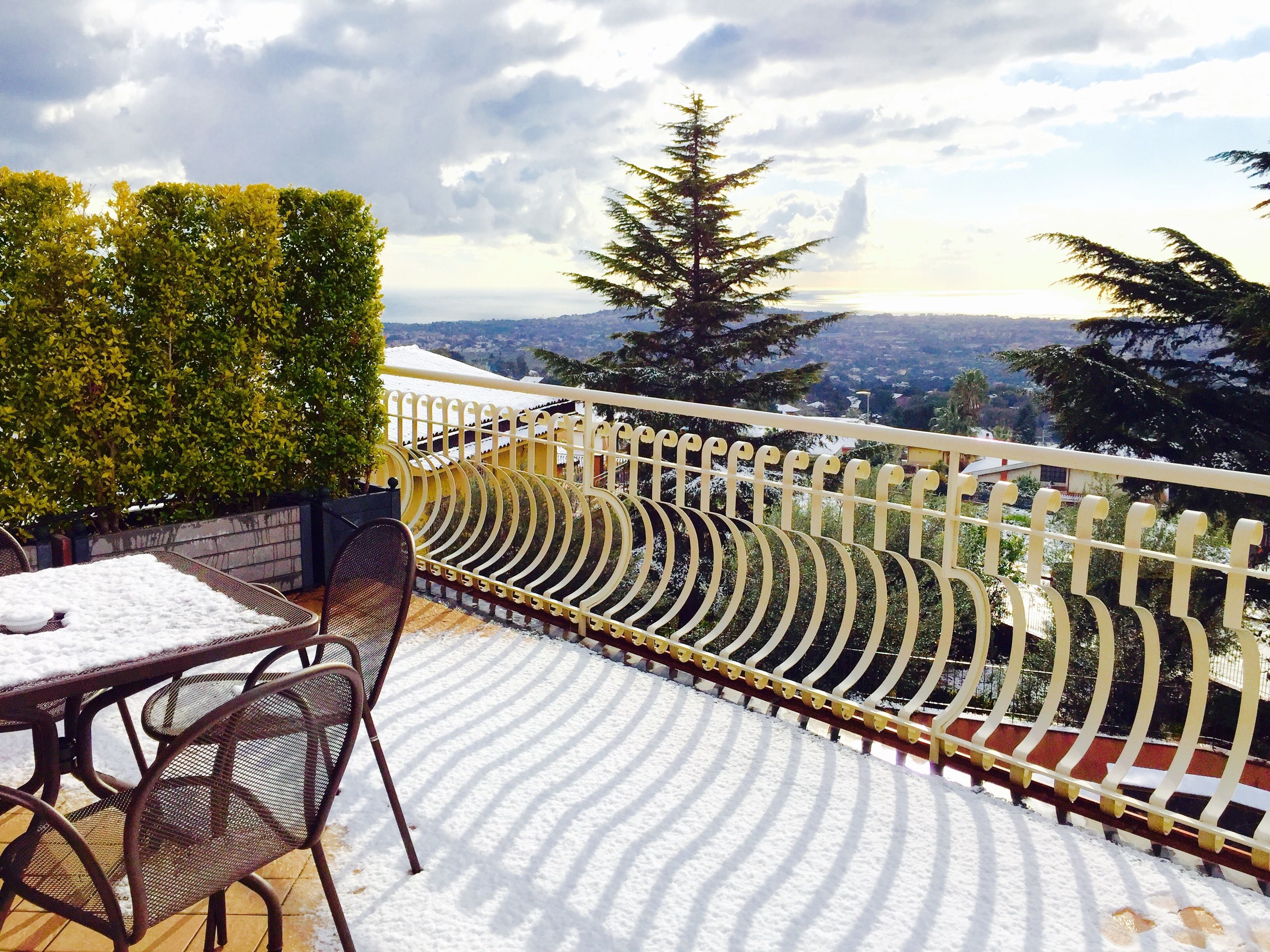 A balcony with a metal table and chairs, a white railing, and a view of a snow-covered landscape.