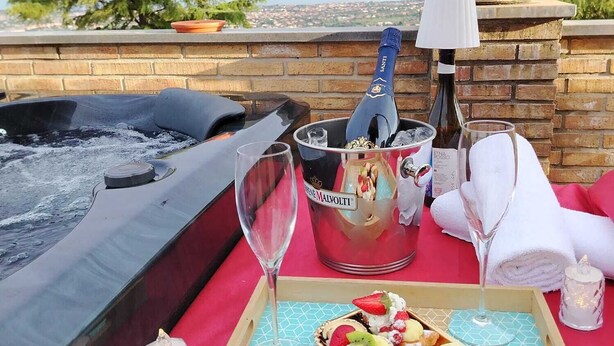 A hot tub with a tray of desserts and drinks, a potted plant, and a view of the city.