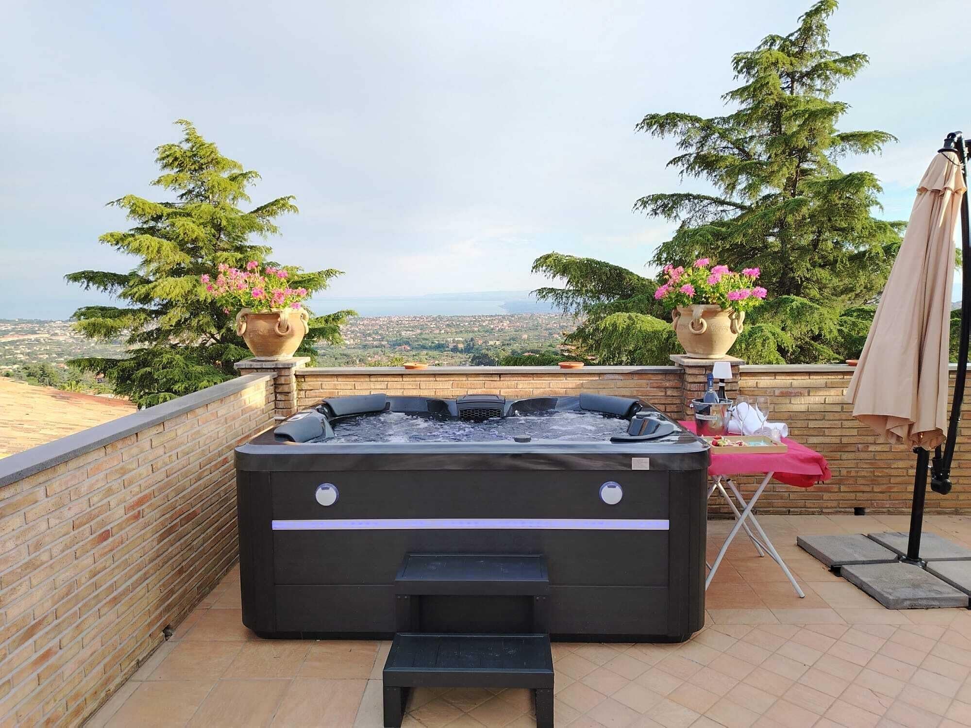 A hot tub with a view of a cityscape, surrounded by potted plants and a table with a red tablecloth.