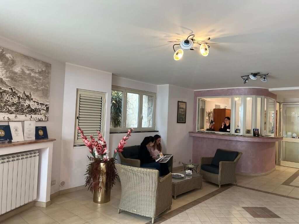 A reception area with a counter, two wicker sofas, a vase with flowers, and a ceiling fan.