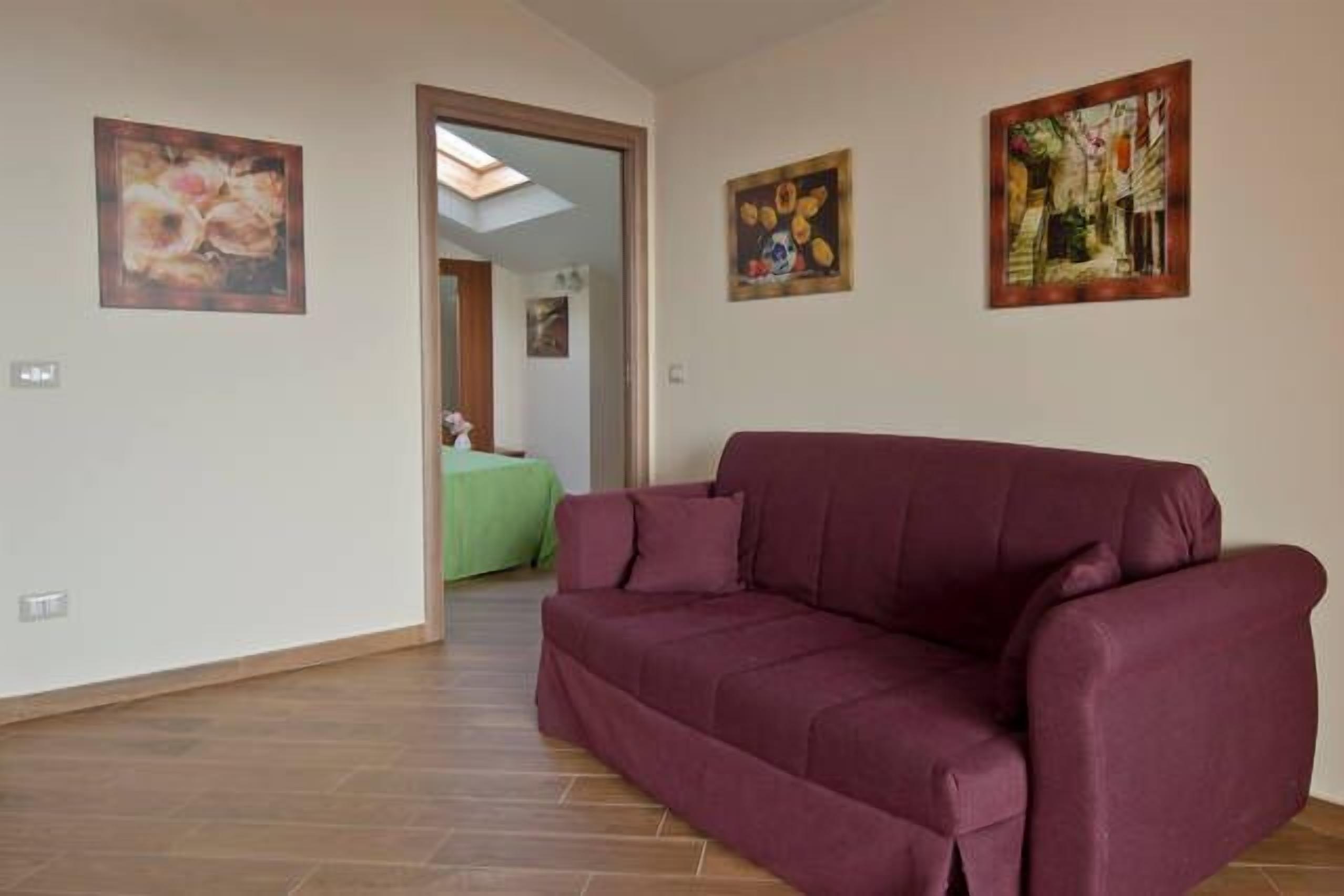 Un soggiorno con un divano color borgogna, un divano verde sullo sfondo e due quadri alle pareti.