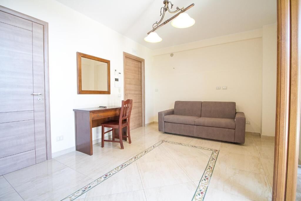 Um quarto com uma escrivaninha de madeira, um sofá marrom, um espelho e uma porta.