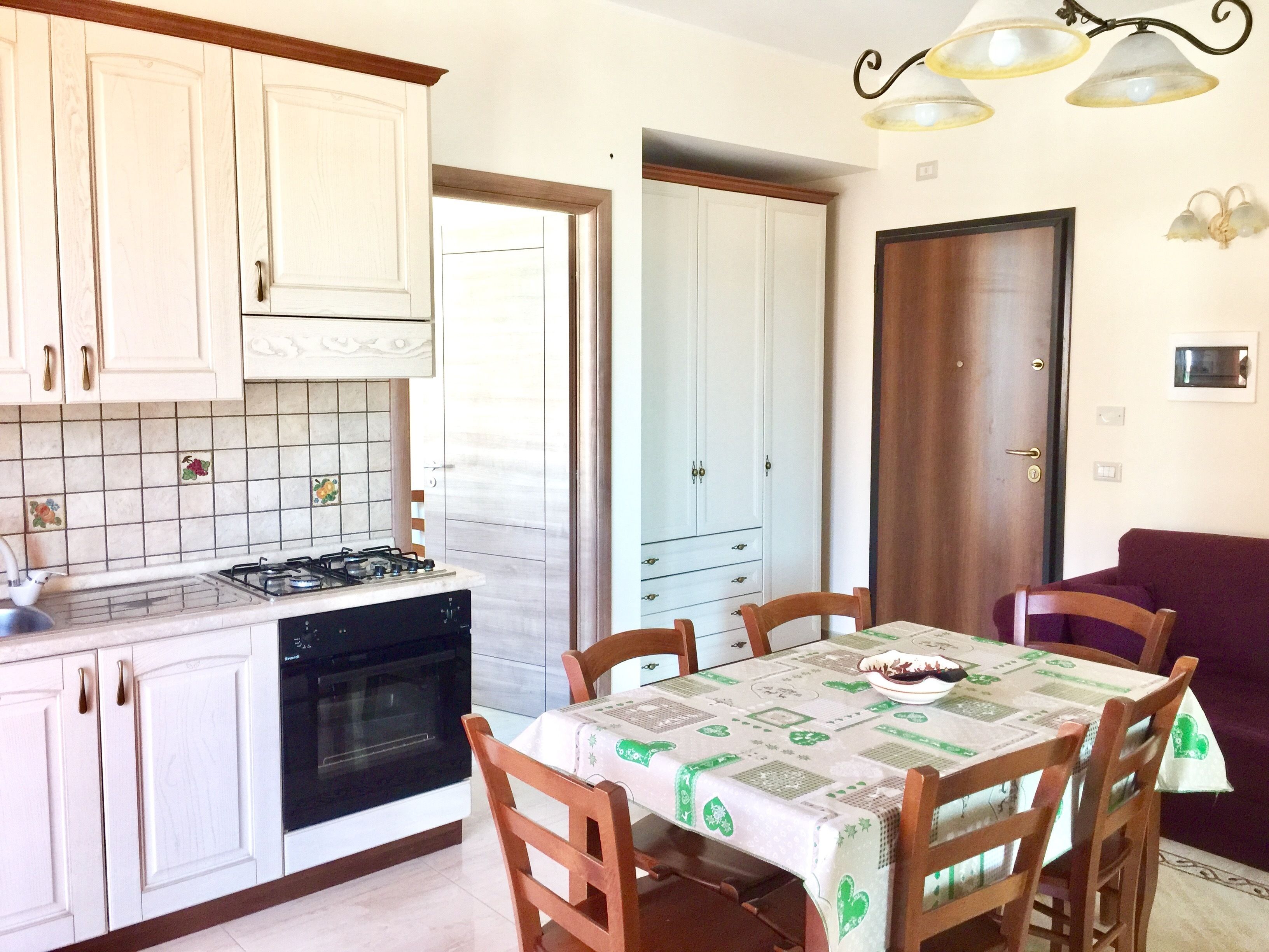 Una cocina con alacenas blancas, una estufa a gas y una mesa de comedor con sillas.