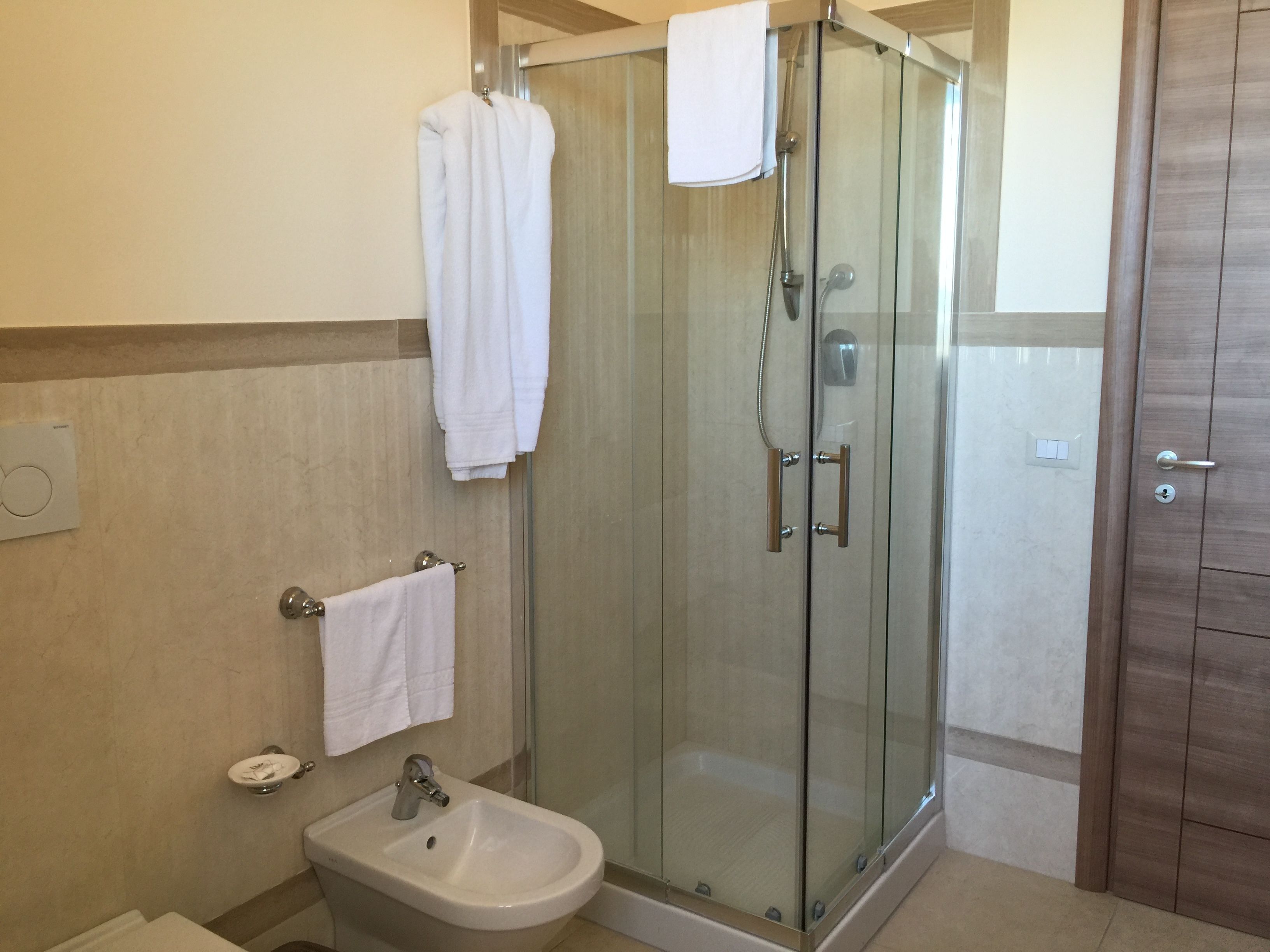 Ein modernes Badezimmer mit einer Glaskabine zur Dusche, einem Bidet und einem Handtuchhalter.