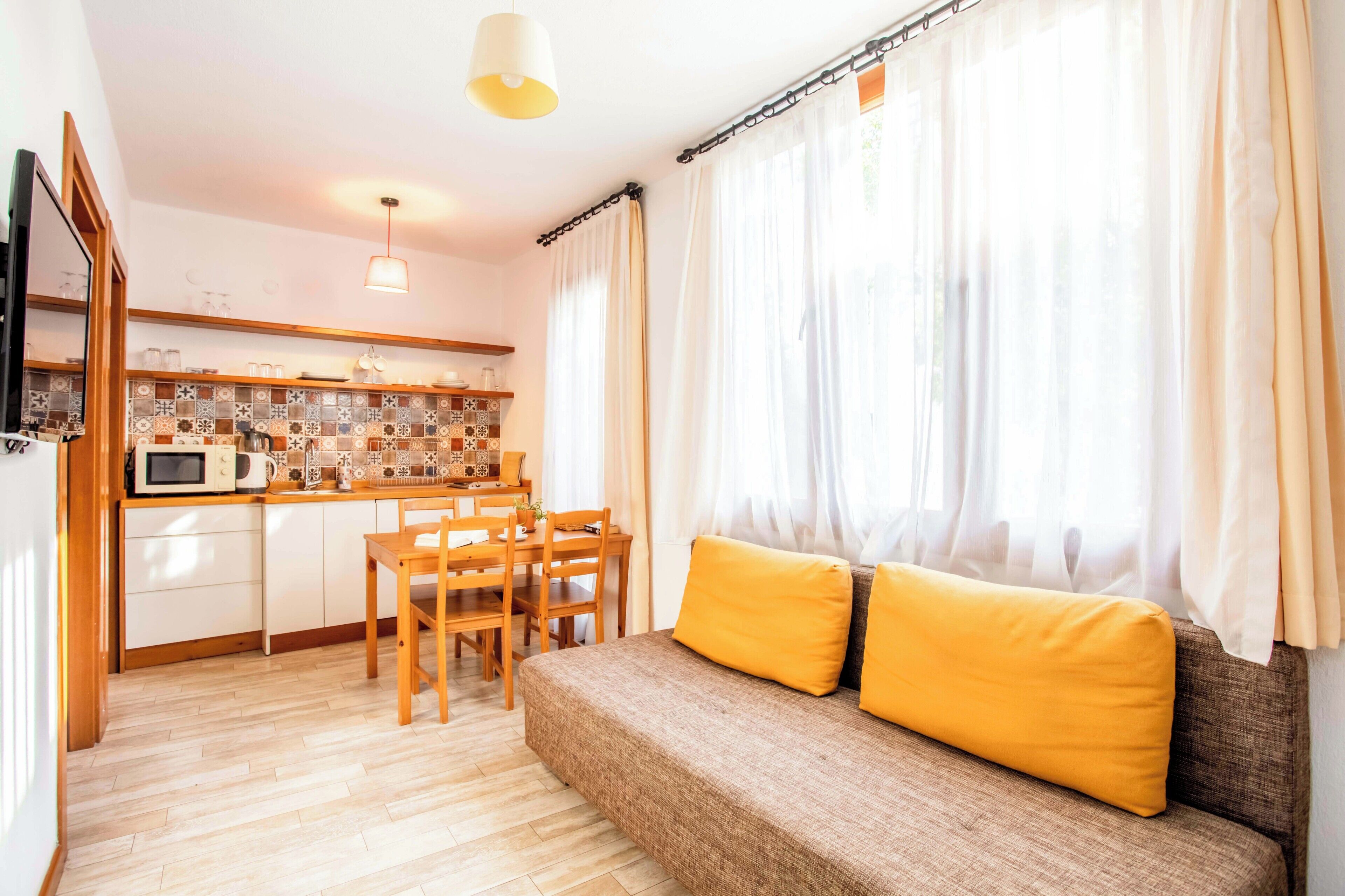 A compact living space with a kitchenette, a dining area, and a sofa with yellow cushions.