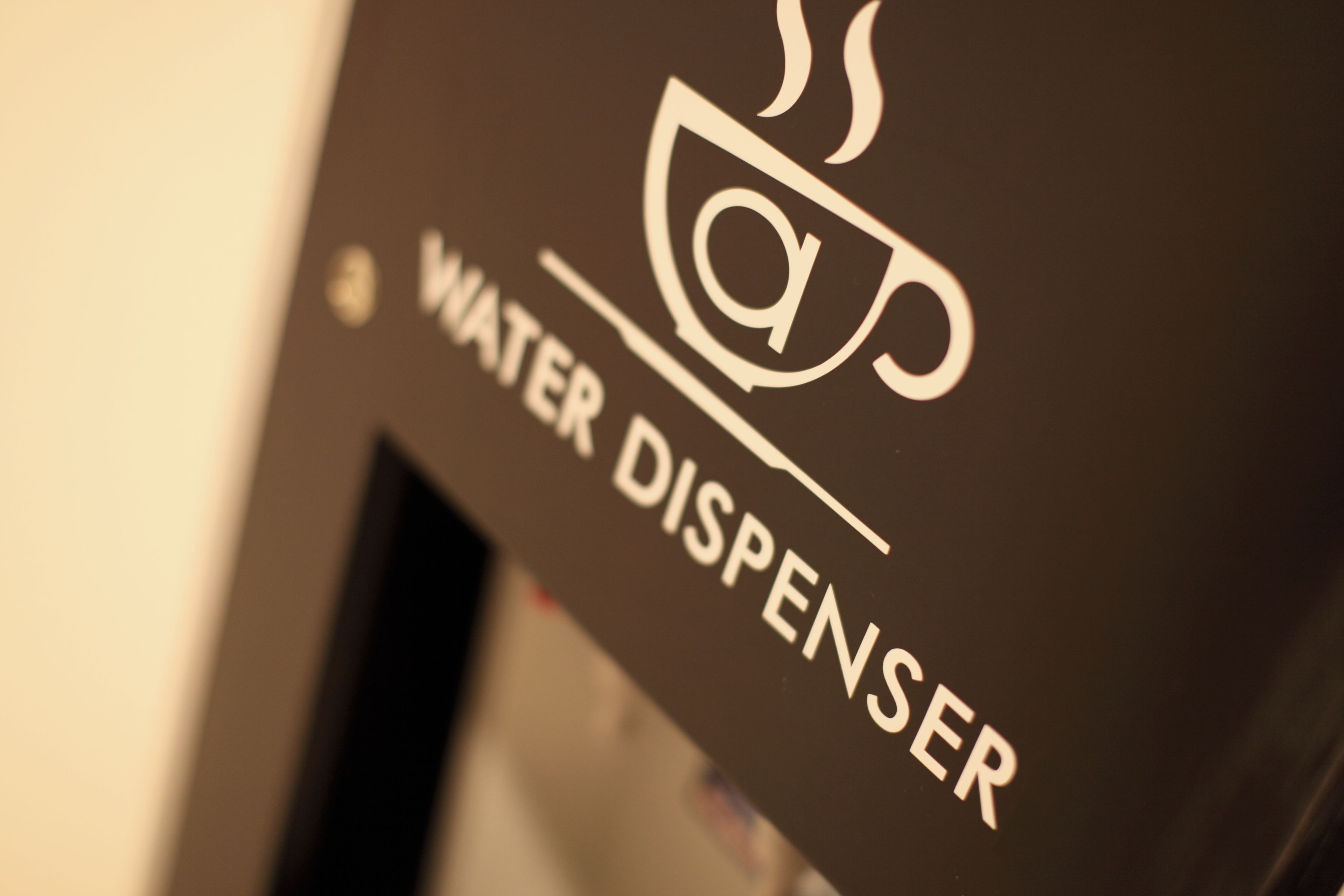 A close-up of a water dispenser with a cup and steam icon, indicating it dispenses hot water.