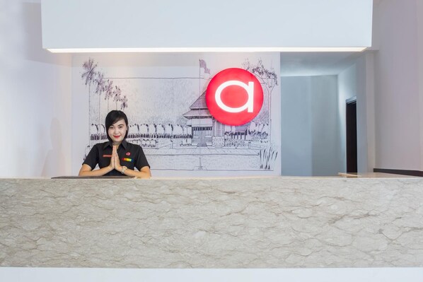 A reception desk with a person standing behind it, a large red logo, and a detailed black and white mural of a traditional building.